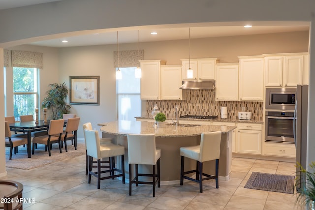 kitchen with pendant lighting, decorative backsplash, an island with sink, appliances with stainless steel finishes, and white cabinetry