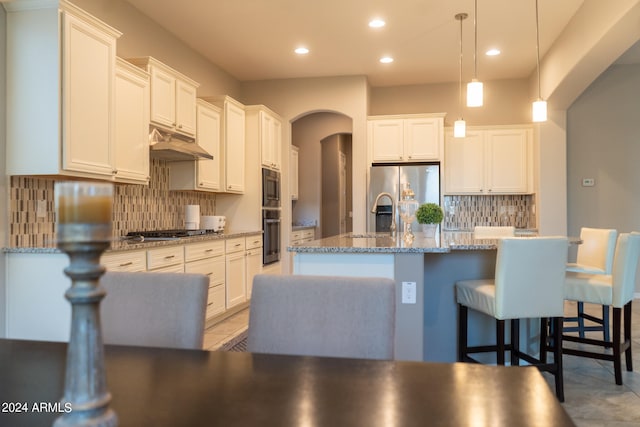 kitchen featuring white cabinets, a center island with sink, hanging light fixtures, tasteful backsplash, and stainless steel appliances