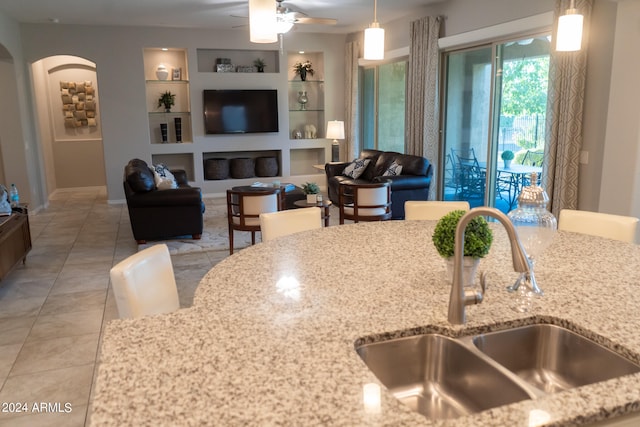 kitchen with light stone counters, built in shelves, ceiling fan, sink, and light tile patterned flooring