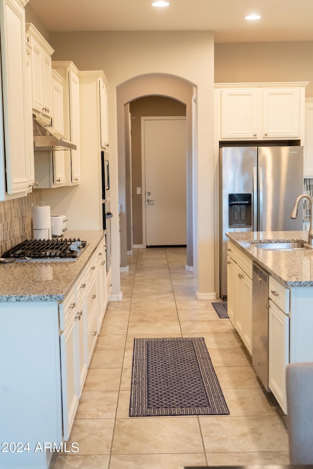 kitchen with light stone countertops, backsplash, stainless steel appliances, and white cabinetry