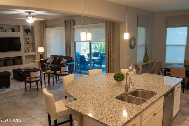 kitchen with a kitchen bar, built in shelves, a kitchen island with sink, sink, and hanging light fixtures