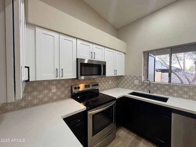 kitchen with sink, backsplash, stainless steel appliances, light hardwood / wood-style floors, and white cabinets