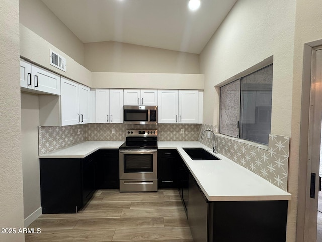 kitchen with lofted ceiling, sink, appliances with stainless steel finishes, backsplash, and white cabinets