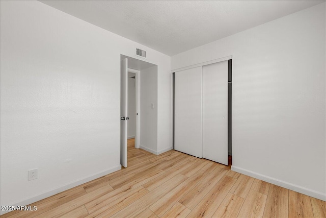 unfurnished bedroom with baseboards, visible vents, wood-type flooring, and a closet