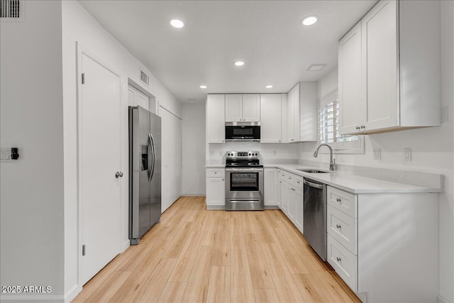 kitchen featuring visible vents, light wood-style flooring, a sink, stainless steel appliances, and white cabinetry