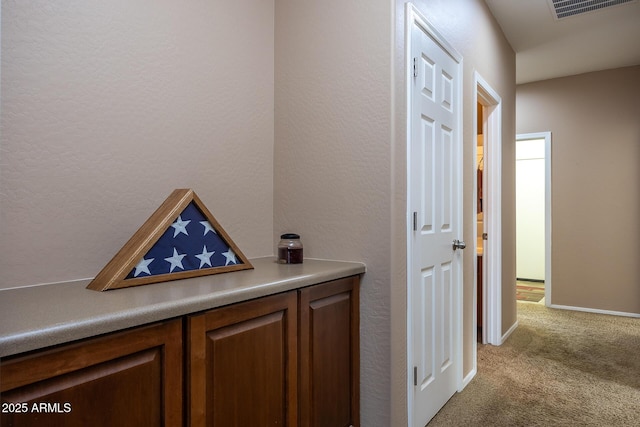 corridor featuring a textured wall, carpet floors, visible vents, and baseboards