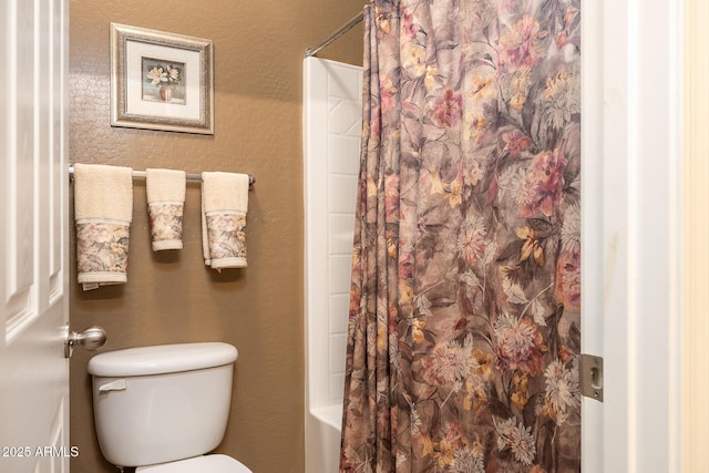 bathroom featuring shower / tub combo, a textured wall, and toilet