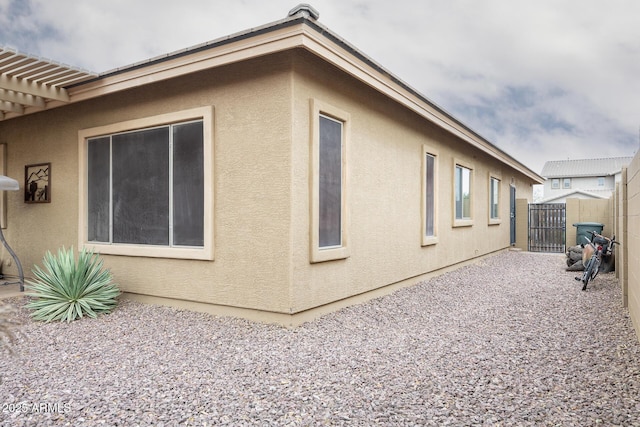 view of side of property with fence, a gate, and stucco siding