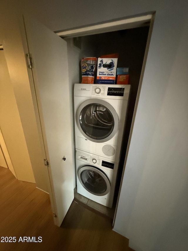 clothes washing area featuring stacked washer and dryer, laundry area, and dark wood-type flooring