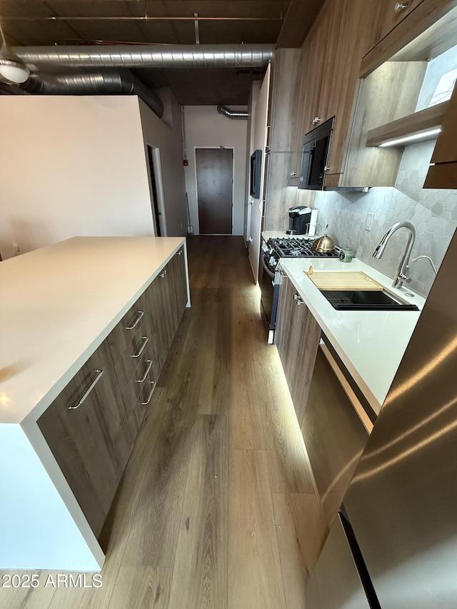 kitchen with dark wood-style floors, modern cabinets, stainless steel range with gas cooktop, black microwave, and a sink