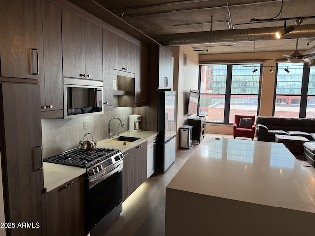 kitchen with dark brown cabinetry, a sink, light countertops, appliances with stainless steel finishes, and decorative backsplash