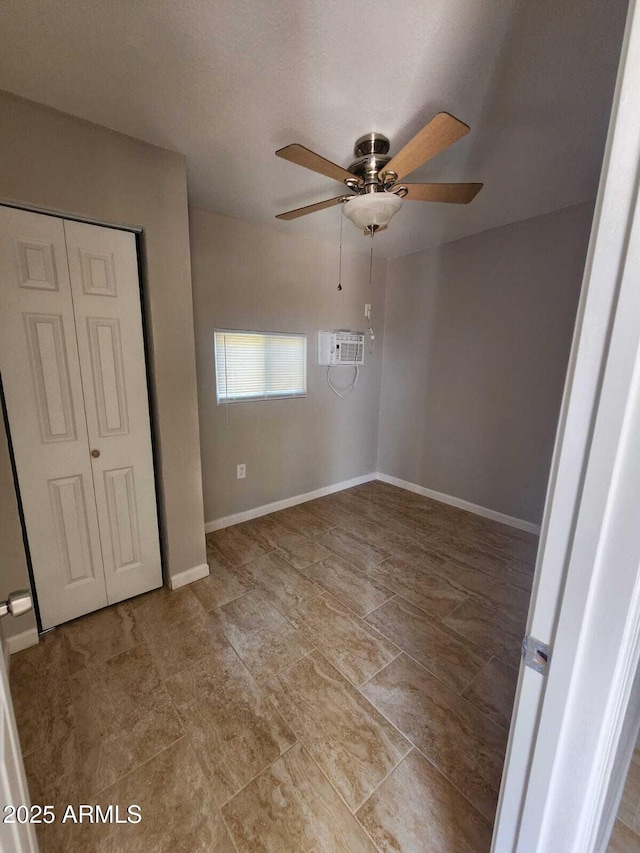 unfurnished bedroom with an AC wall unit, a closet, a ceiling fan, and baseboards