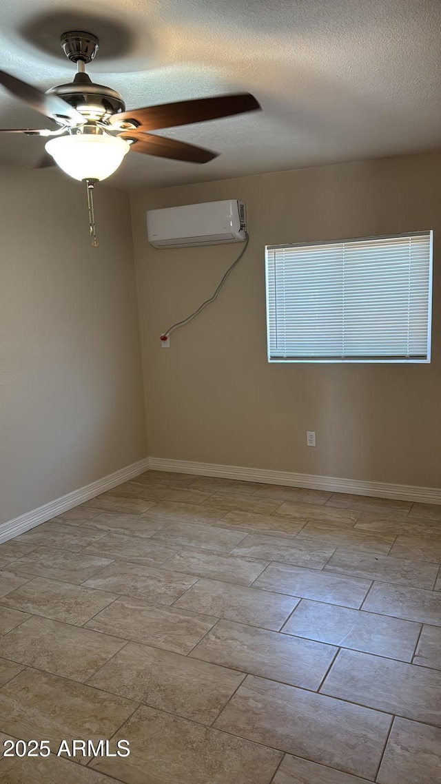 spare room with a textured ceiling, baseboards, a ceiling fan, and an AC wall unit