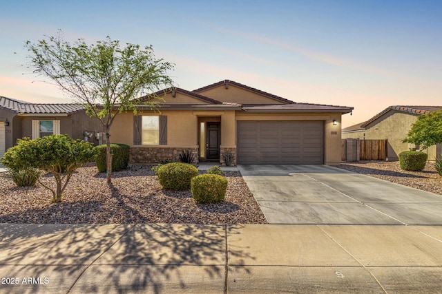 ranch-style house with stucco siding, stone siding, fence, concrete driveway, and a garage