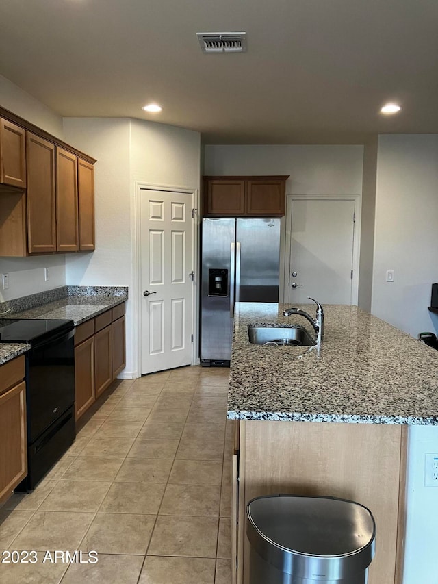 kitchen with an island with sink, black range with electric stovetop, dark stone countertops, and sink