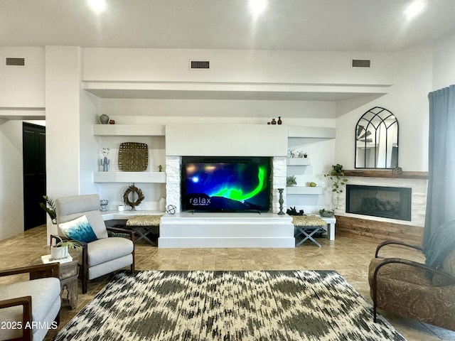 living area featuring visible vents, built in features, and a glass covered fireplace