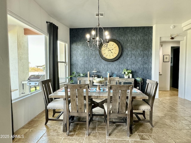 dining area with a chandelier, an accent wall, stone tile floors, and wallpapered walls