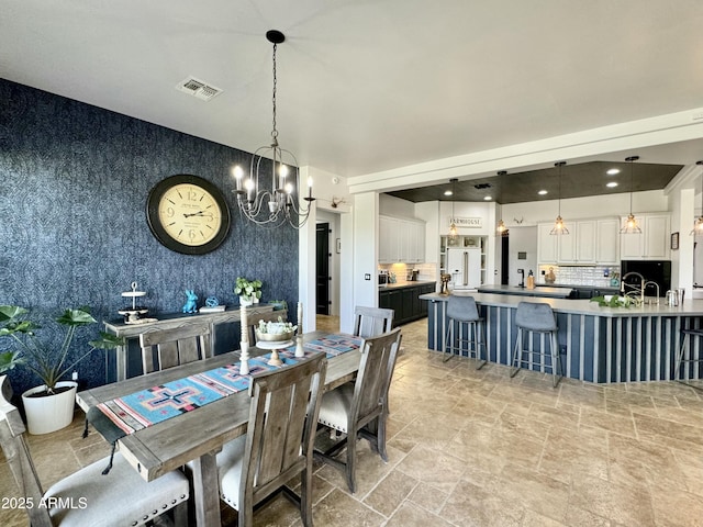 dining room featuring stone finish flooring, visible vents, a notable chandelier, and wallpapered walls