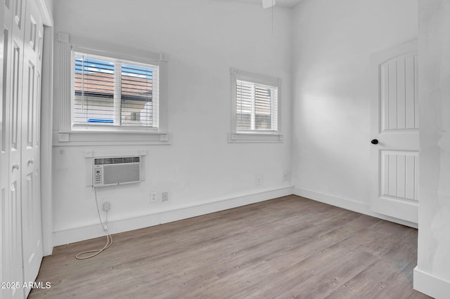 empty room with a wall mounted AC, baseboards, and wood finished floors