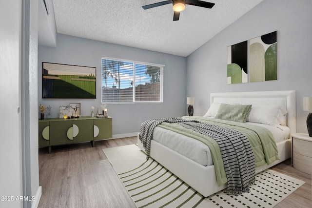 bedroom with a ceiling fan, vaulted ceiling, a textured ceiling, wood finished floors, and baseboards