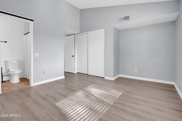 unfurnished bedroom with baseboards, visible vents, connected bathroom, wood finished floors, and vaulted ceiling