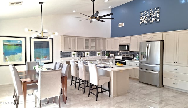 kitchen with a high ceiling, pendant lighting, stainless steel appliances, tasteful backsplash, and a breakfast bar