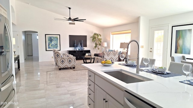 kitchen with stainless steel appliances, ceiling fan, sink, vaulted ceiling, and light stone counters