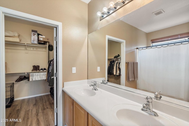 bathroom featuring a walk in closet, wood finished floors, a sink, and double vanity