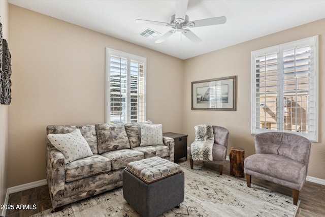 living area featuring baseboards, wood finished floors, visible vents, and a ceiling fan