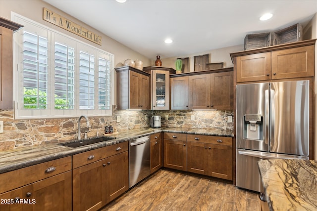 kitchen with dark wood-style flooring, tasteful backsplash, appliances with stainless steel finishes, a sink, and dark stone countertops