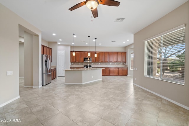 kitchen with visible vents, backsplash, appliances with stainless steel finishes, a kitchen island with sink, and baseboards