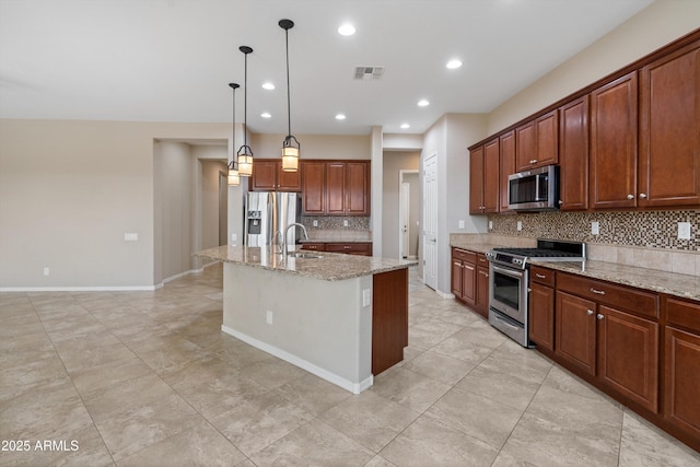 kitchen featuring a center island with sink, appliances with stainless steel finishes, light stone countertops, pendant lighting, and a sink