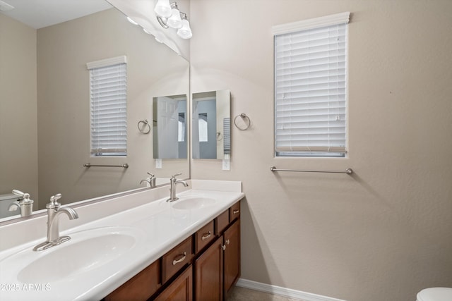 bathroom featuring toilet, double vanity, baseboards, and a sink