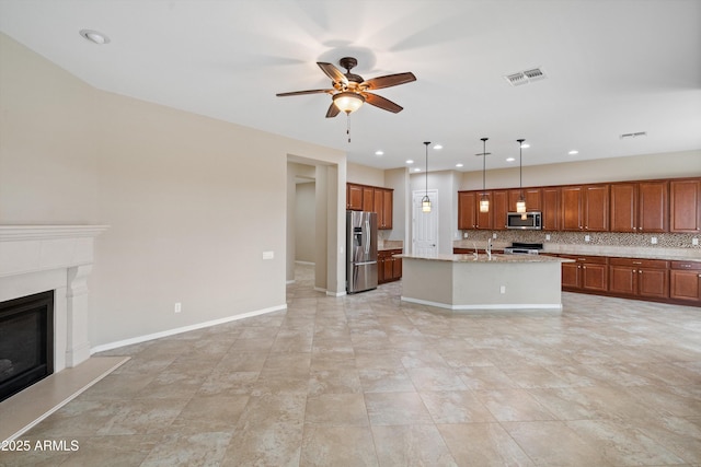 kitchen with visible vents, open floor plan, appliances with stainless steel finishes, decorative backsplash, and a glass covered fireplace