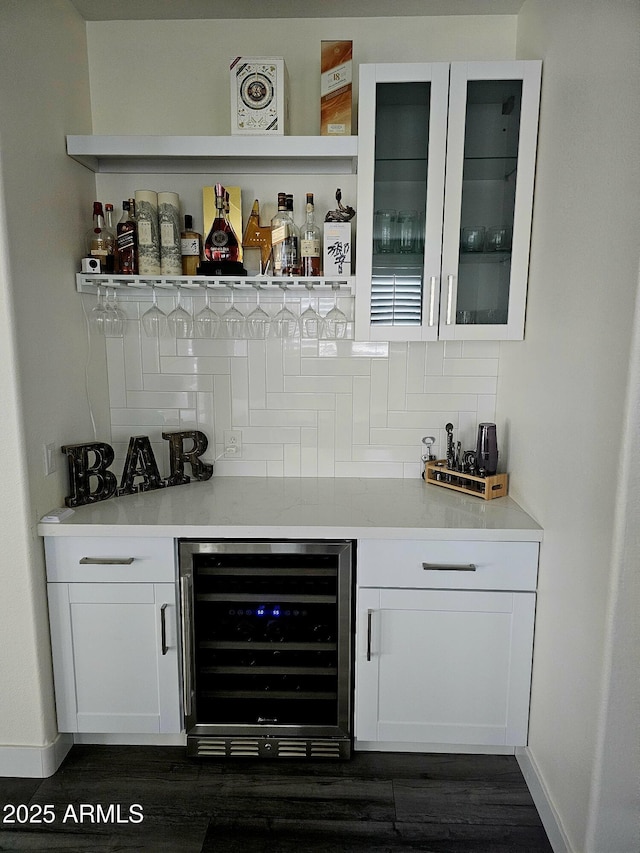 bar featuring dark wood finished floors, decorative backsplash, a bar, beverage cooler, and baseboards