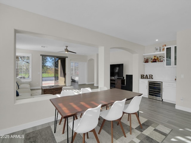 dining space featuring beverage cooler, a dry bar, arched walkways, and light wood-style floors