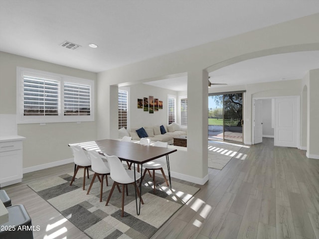 dining room with light wood finished floors, visible vents, arched walkways, and baseboards