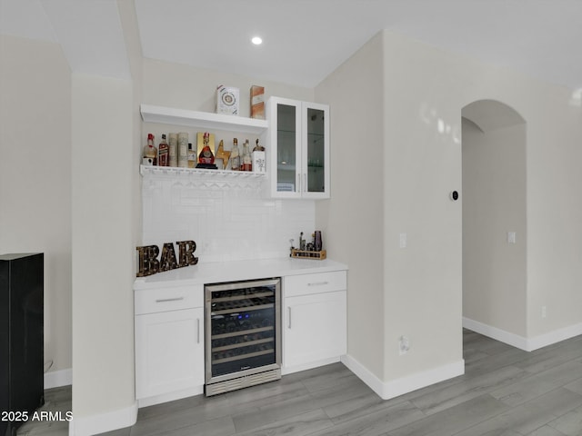 bar with wine cooler, baseboards, light wood-type flooring, decorative backsplash, and a bar