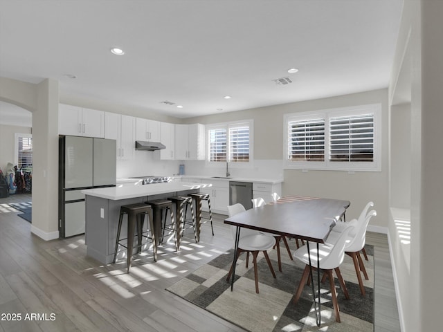 dining room with light wood finished floors, baseboards, visible vents, arched walkways, and recessed lighting