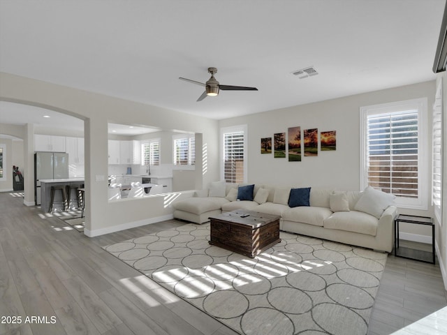 living room featuring arched walkways, visible vents, ceiling fan, and light wood finished floors