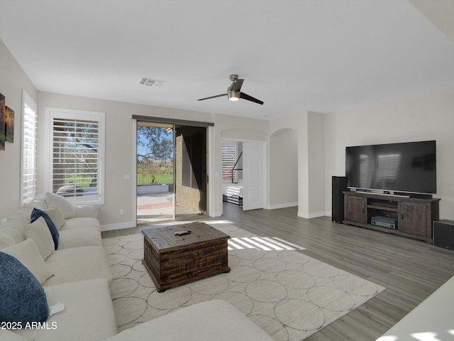 living area with arched walkways, ceiling fan, wood finished floors, visible vents, and baseboards