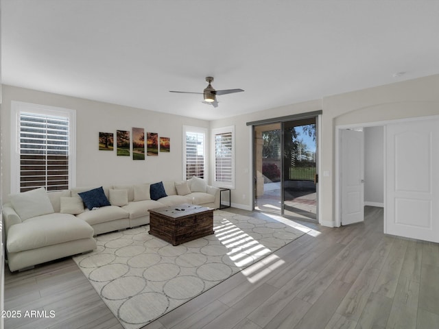 living area featuring light wood-style floors, baseboards, and a ceiling fan