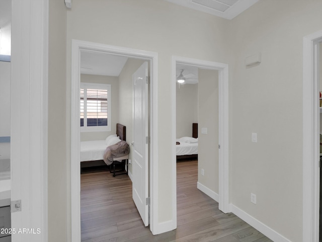 hall with attic access, wood finished floors, visible vents, and baseboards