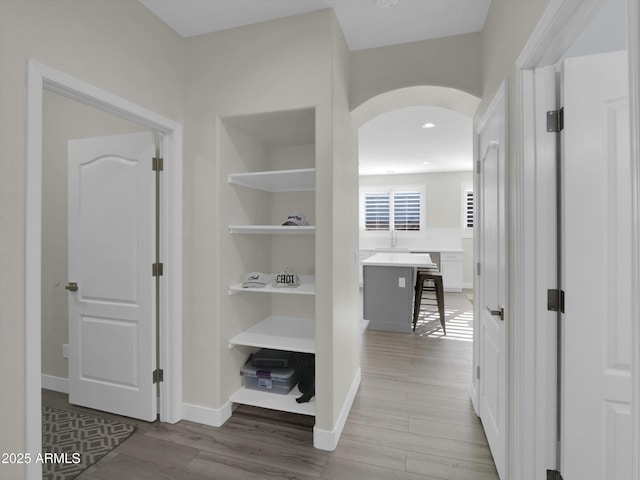 hall with arched walkways, wood finished floors, and baseboards