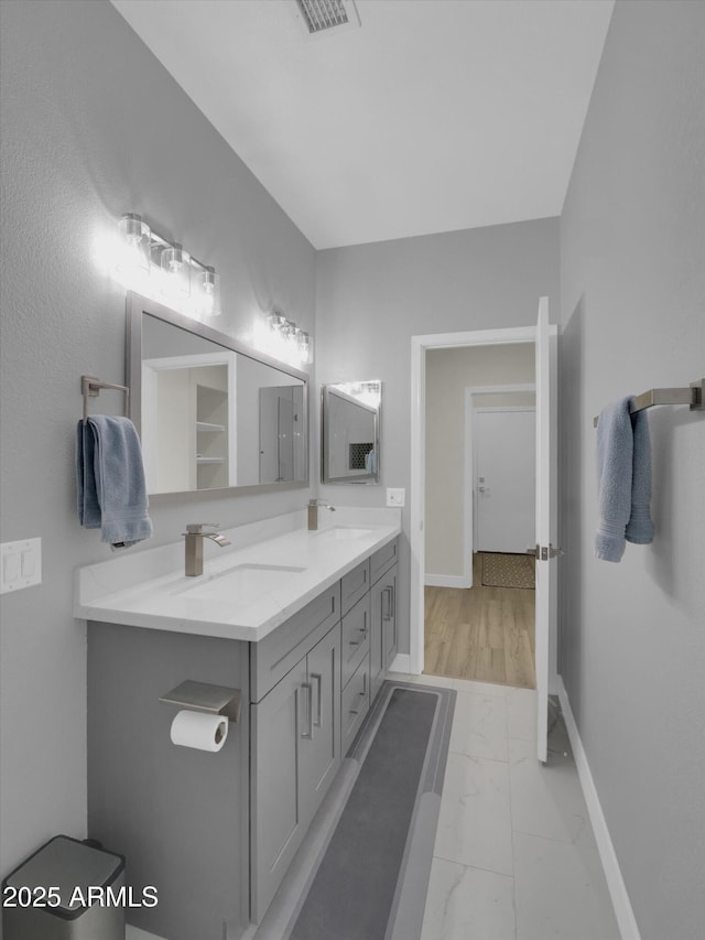 full bath with marble finish floor, a sink, baseboards, and double vanity