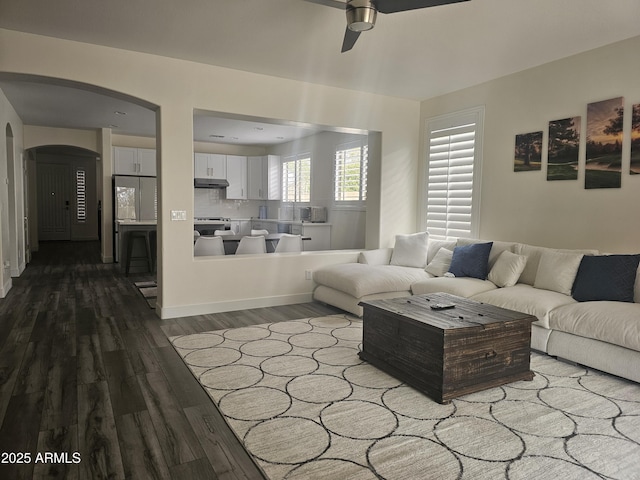 living area with arched walkways, ceiling fan, and wood finished floors