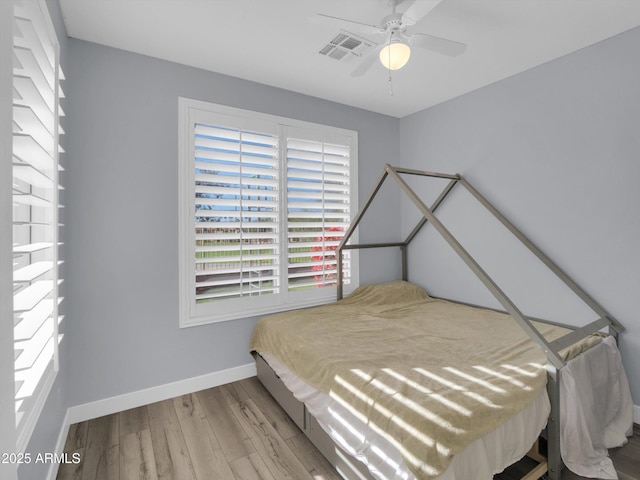 bedroom with a ceiling fan, visible vents, baseboards, and wood finished floors