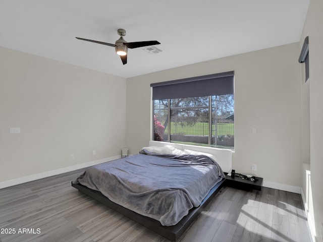 bedroom with a ceiling fan, visible vents, baseboards, and wood finished floors