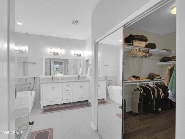 bathroom with marble finish floor, visible vents, a freestanding tub, and vanity