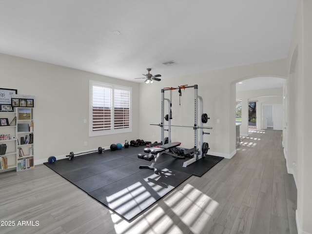 exercise area featuring baseboards, visible vents, arched walkways, and wood finished floors